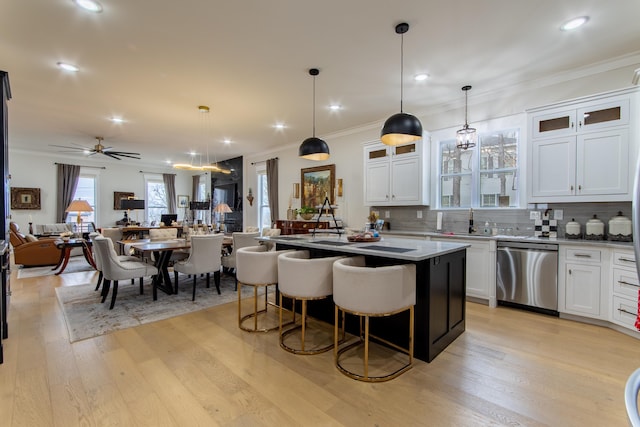 kitchen featuring white cabinetry, dishwasher, an island with sink, a kitchen bar, and hanging light fixtures