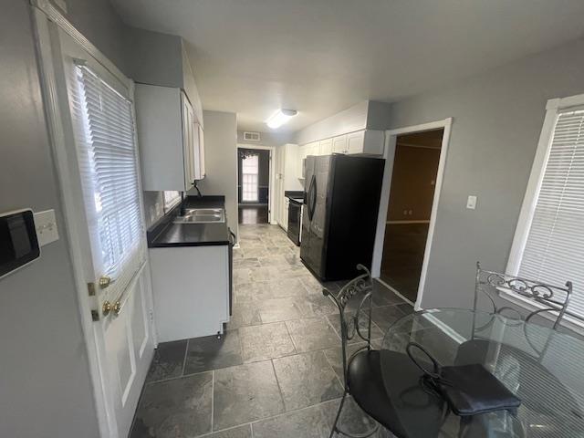 kitchen with black refrigerator, sink, electric range oven, and white cabinets