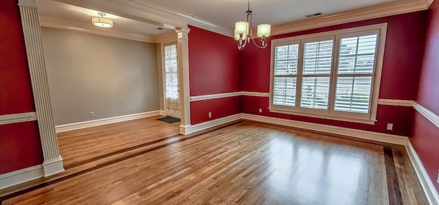 spare room with ornate columns, crown molding, hardwood / wood-style floors, and an inviting chandelier