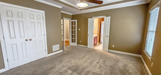 unfurnished bedroom featuring light colored carpet, ornamental molding, a tray ceiling, and multiple windows