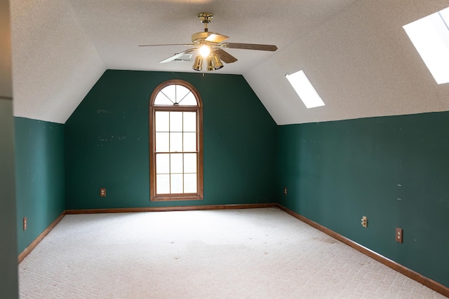 additional living space with ceiling fan, carpet floors, vaulted ceiling with skylight, and a textured ceiling