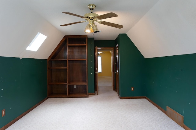 additional living space with ceiling fan, built in features, light colored carpet, and vaulted ceiling with skylight