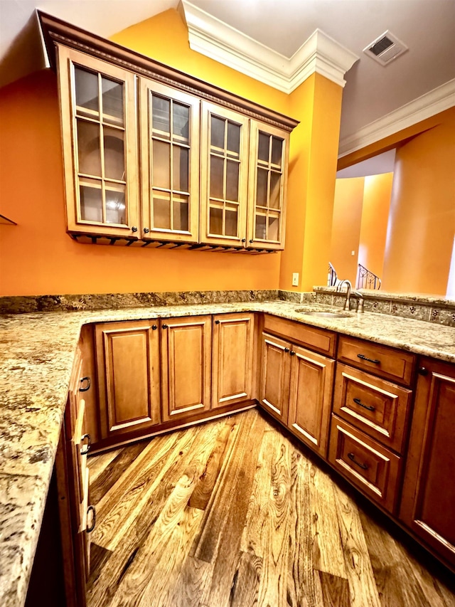 kitchen with light stone counters, ornamental molding, light hardwood / wood-style floors, and sink