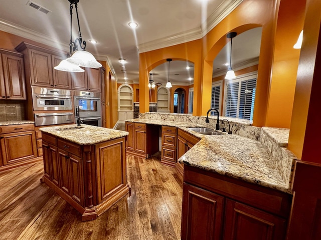 kitchen featuring sink, a kitchen island with sink, pendant lighting, and stainless steel double oven