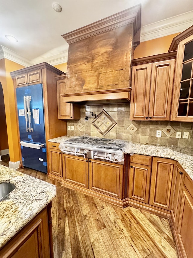 kitchen featuring stainless steel gas cooktop, fridge, ornamental molding, light stone countertops, and light hardwood / wood-style floors