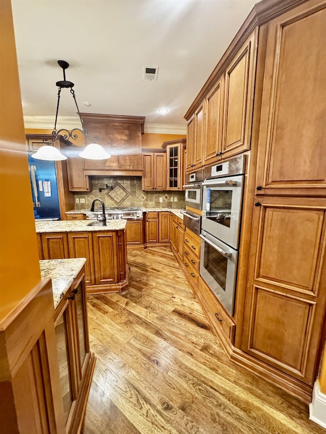 kitchen featuring appliances with stainless steel finishes, decorative light fixtures, light stone counters, crown molding, and light wood-type flooring