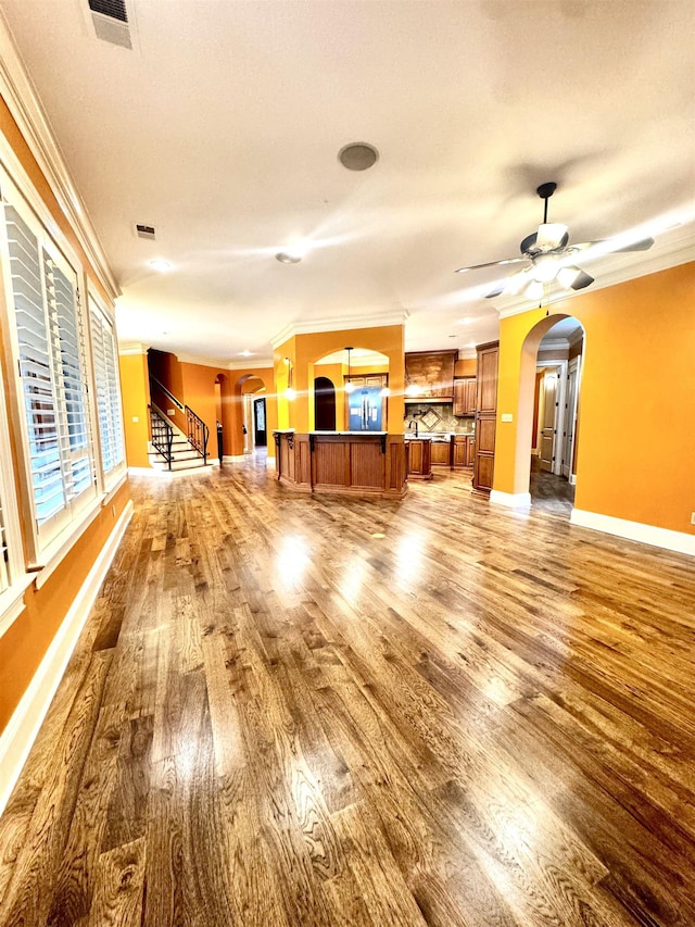 unfurnished living room featuring hardwood / wood-style flooring, ornamental molding, and ceiling fan