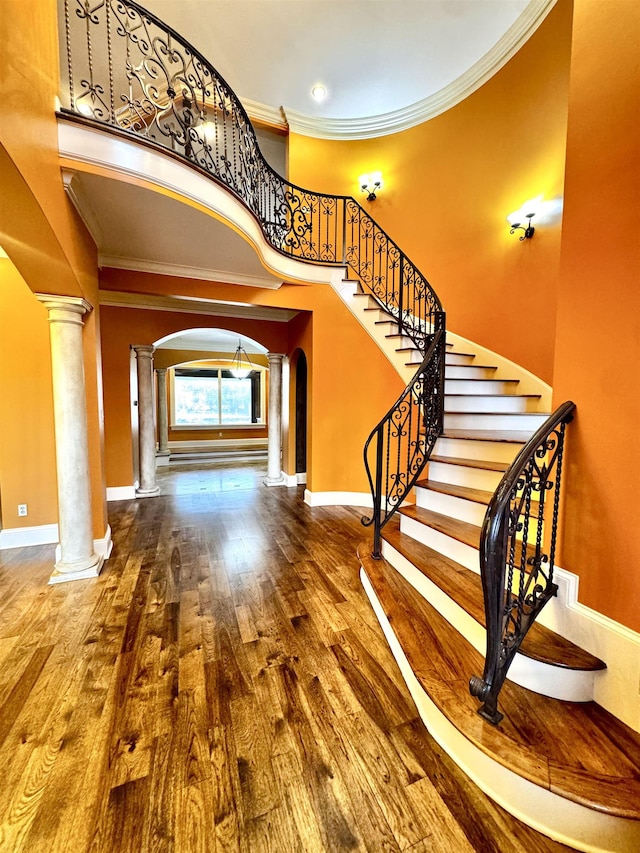 stairs featuring decorative columns, wood-type flooring, ornamental molding, and a towering ceiling