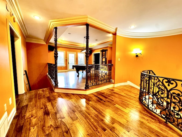 hall with a tray ceiling, wood-type flooring, and ornamental molding