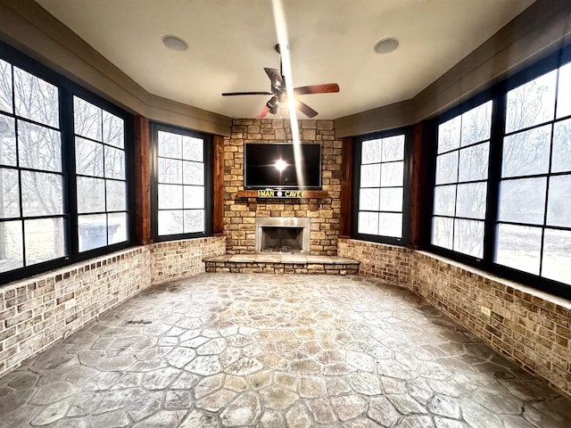 unfurnished living room with brick wall, a stone fireplace, and ceiling fan