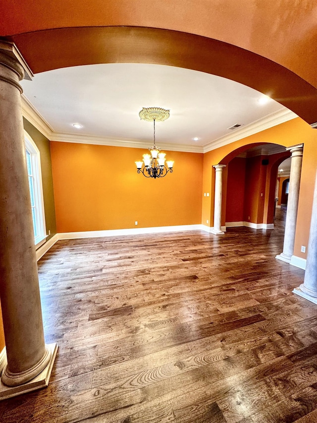 empty room with hardwood / wood-style floors, crown molding, decorative columns, and a chandelier