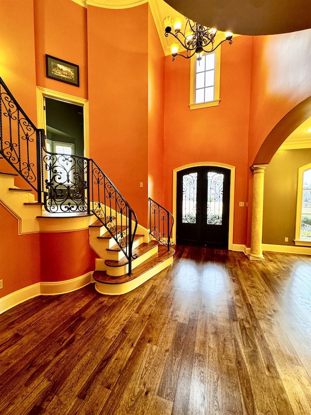 foyer featuring french doors, wood-type flooring, a chandelier, ornamental molding, and a high ceiling