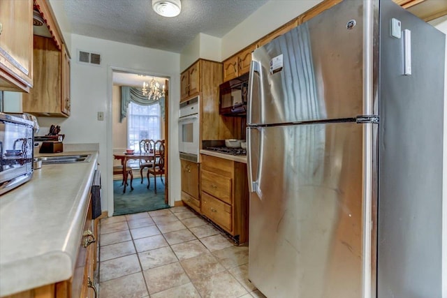 kitchen featuring stainless steel refrigerator, oven, light tile patterned floors, a notable chandelier, and a textured ceiling