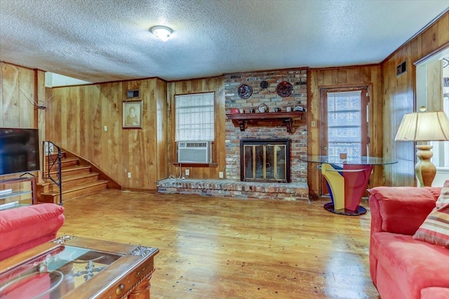 living room with hardwood / wood-style floors, wooden walls, a fireplace, cooling unit, and a textured ceiling