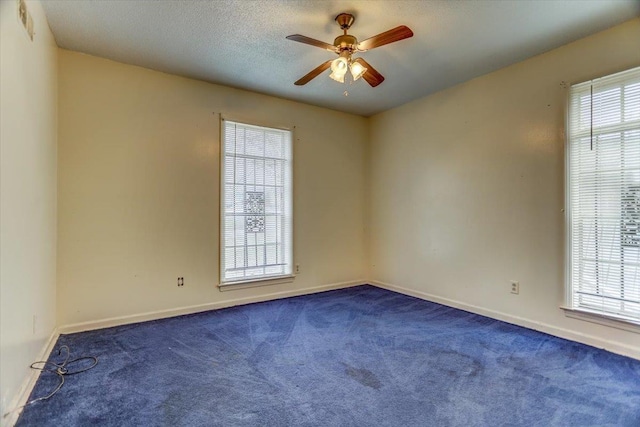 spare room with dark carpet, a wealth of natural light, a textured ceiling, and ceiling fan