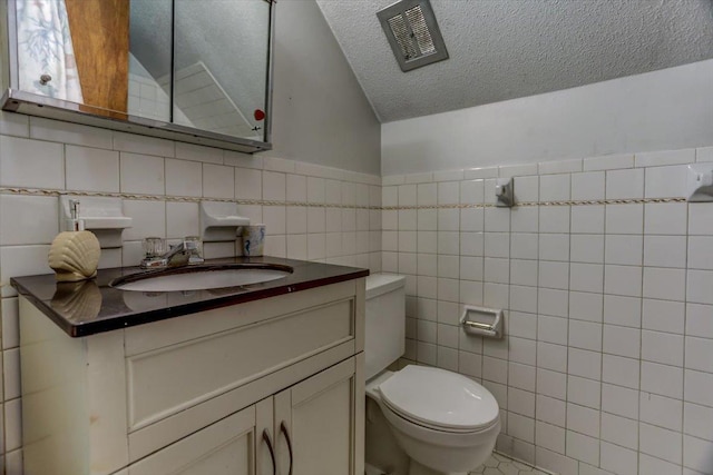 bathroom with vanity, toilet, a textured ceiling, and tile walls