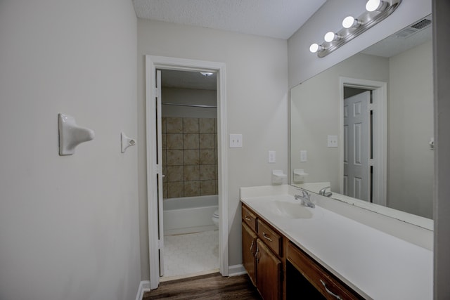 full bathroom with hardwood / wood-style floors, tiled shower / bath combo, vanity, a textured ceiling, and toilet