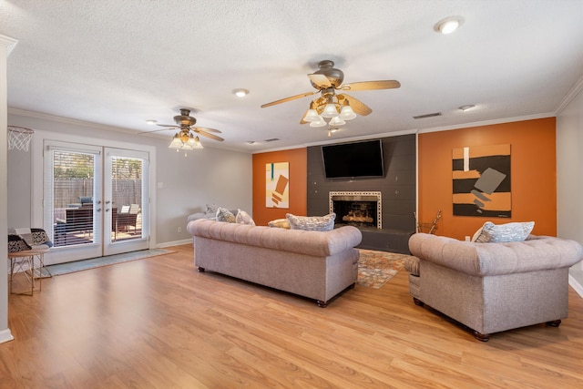 living room featuring crown molding, a large fireplace, light hardwood / wood-style floors, and a textured ceiling