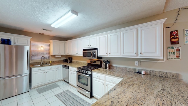 kitchen with sink, appliances with stainless steel finishes, light stone counters, white cabinets, and light tile patterned flooring