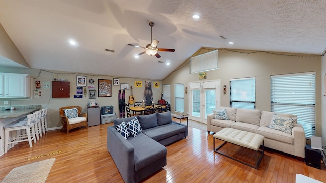 living room featuring lofted ceiling, light wood-type flooring, ceiling fan, a textured ceiling, and french doors