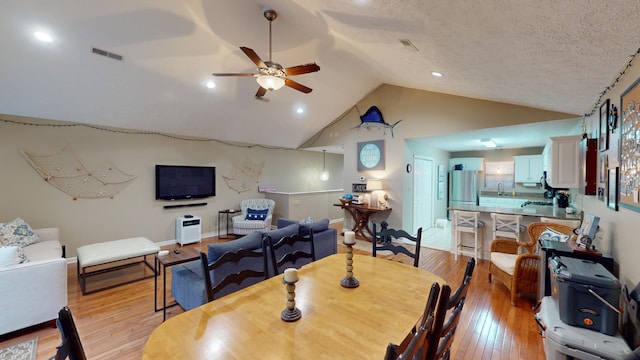 dining area with ceiling fan, lofted ceiling, a textured ceiling, and light hardwood / wood-style floors