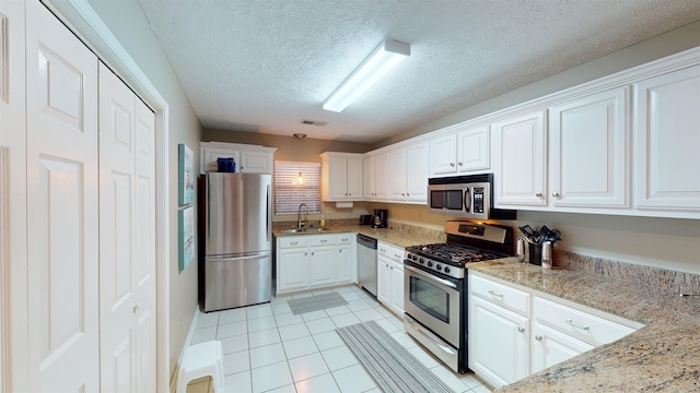 kitchen featuring stainless steel appliances, light stone countertops, sink, and white cabinets