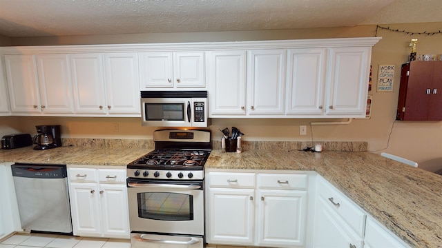 kitchen featuring appliances with stainless steel finishes, light tile patterned floors, a textured ceiling, and white cabinets