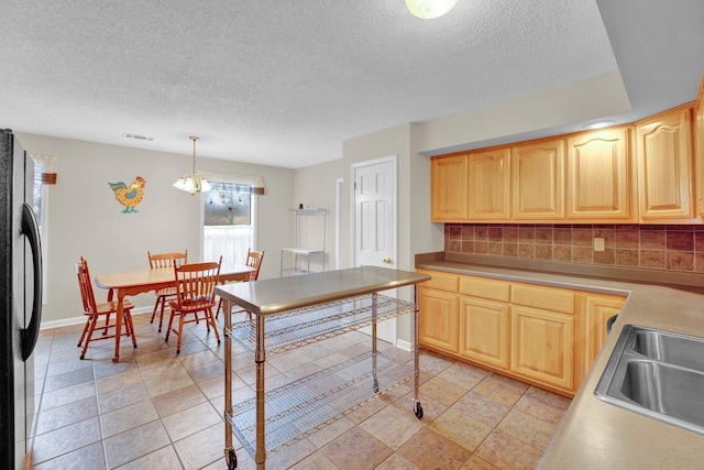 kitchen with black fridge, light brown cabinetry, sink, and hanging light fixtures