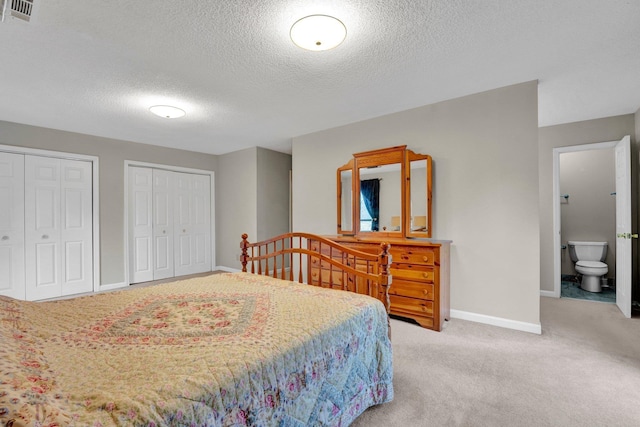 bedroom with light colored carpet, connected bathroom, a textured ceiling, and two closets