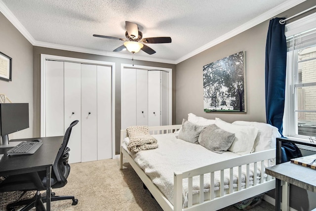 carpeted bedroom featuring ceiling fan, a textured ceiling, ornamental molding, and multiple closets