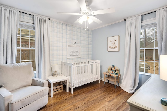 bedroom featuring hardwood / wood-style floors, crown molding, a crib, and ceiling fan