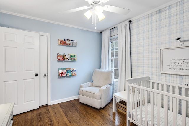 bedroom with crown molding, a crib, dark hardwood / wood-style floors, and ceiling fan