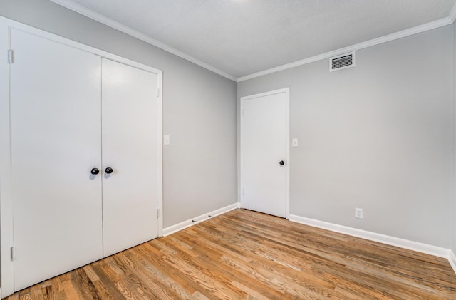 unfurnished bedroom with light hardwood / wood-style flooring, ornamental molding, a closet, and a textured ceiling