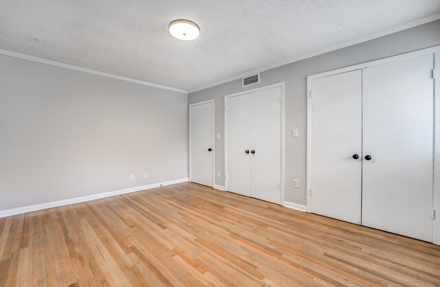 unfurnished bedroom with ornamental molding, light hardwood / wood-style floors, a textured ceiling, and two closets