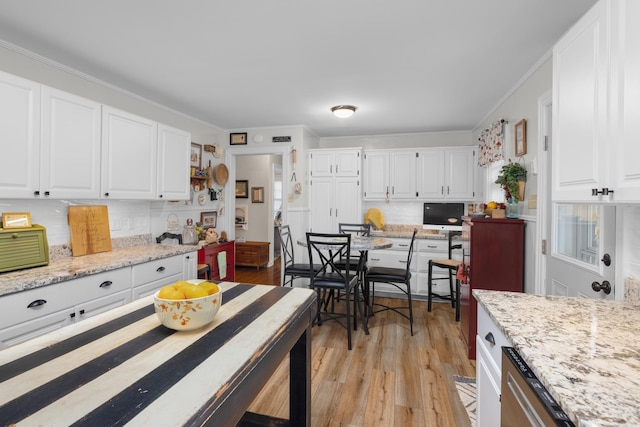 kitchen featuring white cabinetry, light stone counters, ornamental molding, light hardwood / wood-style floors, and decorative backsplash