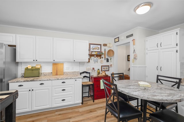 kitchen with white cabinetry, stainless steel fridge, crown molding, light stone countertops, and light wood-type flooring