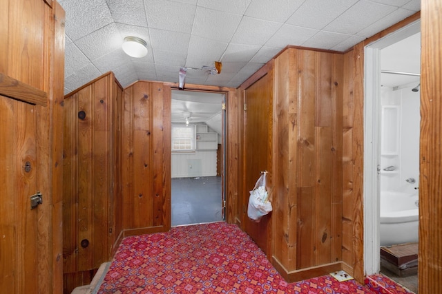 hallway with lofted ceiling and wooden walls