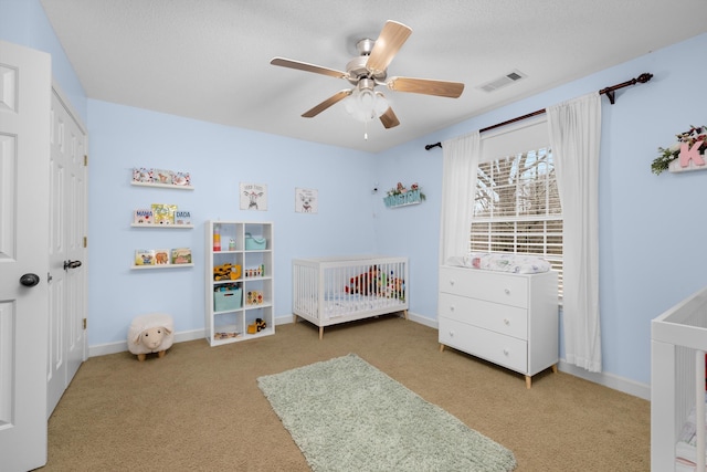 carpeted bedroom with a crib and ceiling fan