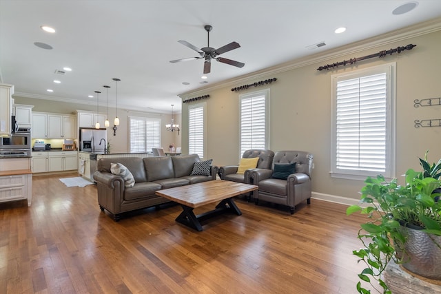 living room featuring crown molding, wood-type flooring, and ceiling fan with notable chandelier