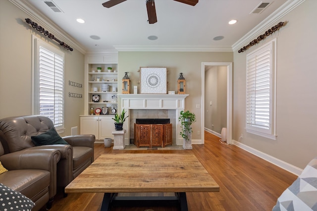 living room with crown molding, light wood-type flooring, built in features, and a fireplace