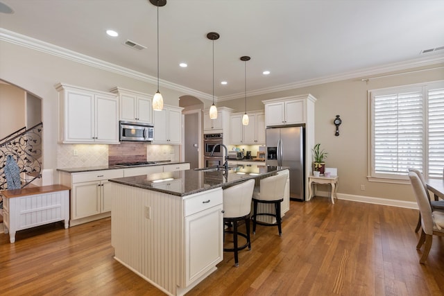 kitchen featuring sink, white cabinetry, decorative light fixtures, appliances with stainless steel finishes, and an island with sink