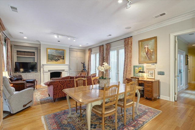 dining space with ornamental molding, track lighting, built in features, and light wood-type flooring