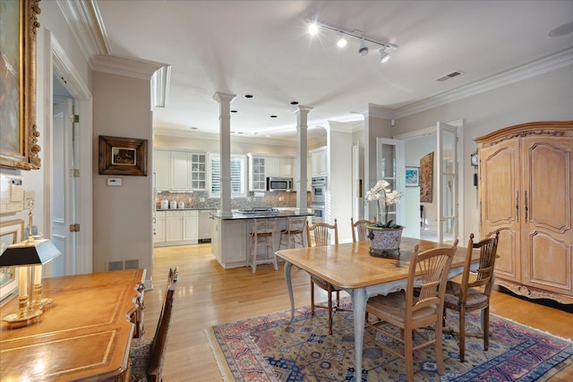 dining area with crown molding, decorative columns, and light hardwood / wood-style flooring