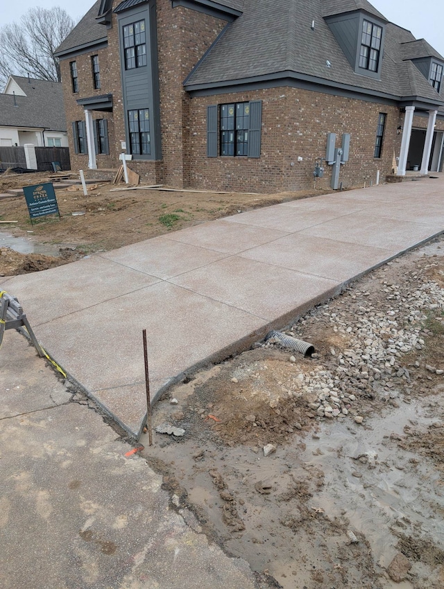 exterior space featuring roof with shingles, concrete driveway, and brick siding