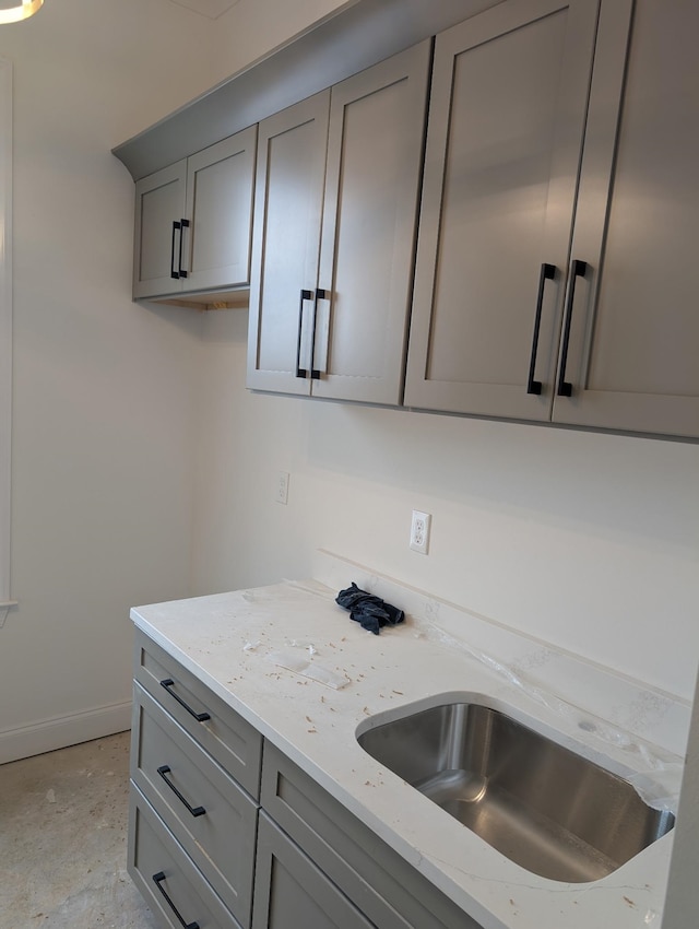 kitchen with sink, gray cabinetry, and light stone counters