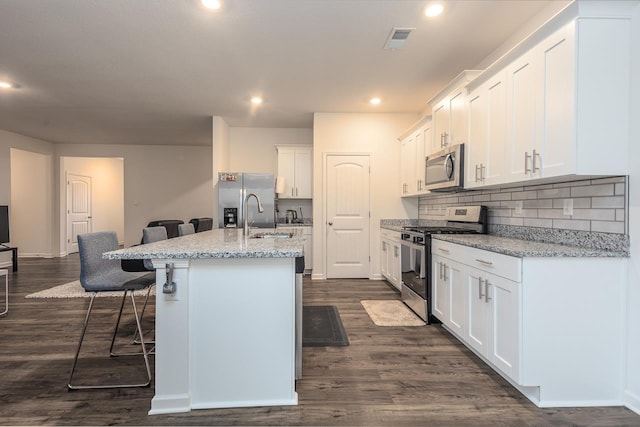 kitchen featuring white cabinetry, a breakfast bar area, stainless steel appliances, light stone countertops, and a center island with sink