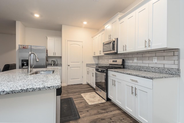 kitchen featuring dark hardwood / wood-style floors, white cabinetry, stainless steel appliances, light stone countertops, and a center island with sink