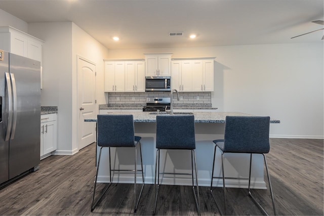 kitchen featuring white cabinetry, a kitchen bar, light stone counters, stainless steel appliances, and a center island with sink