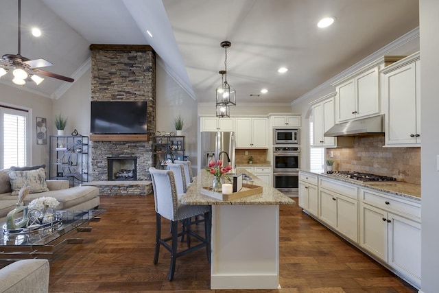 kitchen with pendant lighting, a breakfast bar, stainless steel appliances, light stone counters, and a center island with sink