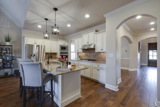 kitchen with sink, light stone counters, appliances with stainless steel finishes, pendant lighting, and a kitchen island with sink